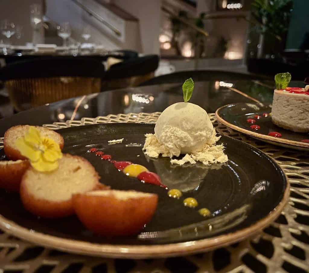 Glulab jamun with ice-cream on. a black plate with mango and summer fruits coulis at Varanasi, Leicester