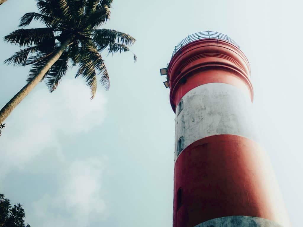 Red and white striped exterior of the Alleppey lighthouse with a palm tree framing the photo