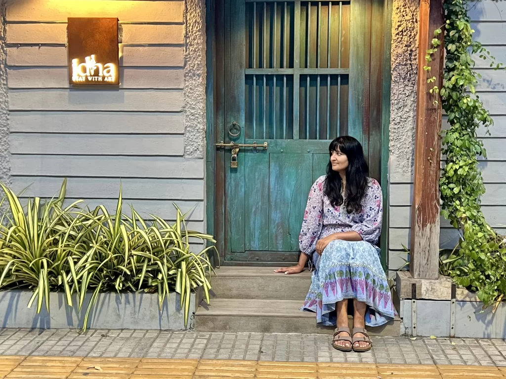 bejal sitting outside a cafe in Fort Kochi wearing a pink and blue floral cotton dress 