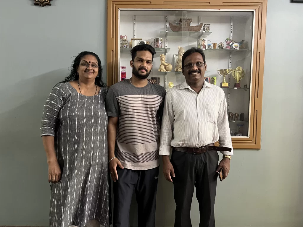 Back 2 Village Mr Suresh family photo. His wife, son and himself in their home standing against a big wall photo