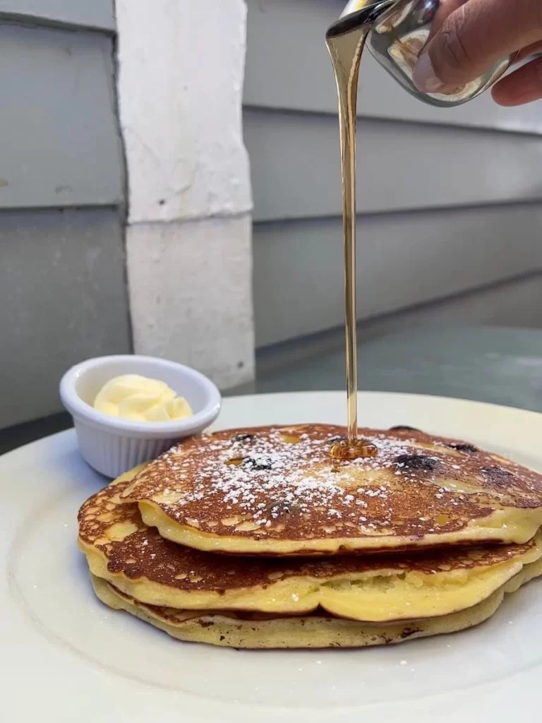 Lemon ricotta pancakes with blueberries and syrup being drizzled over the top at The Cottage La Jolla