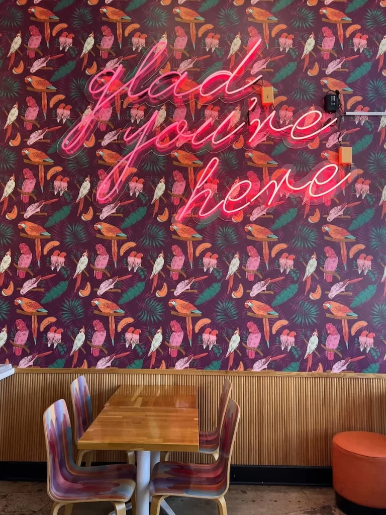 The parakeet bright wall paper with. aneo sign reading, 'glad you're here' at Parakeet Cafe, Coronado, San Diego