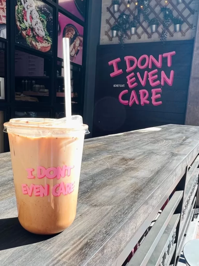Coffee and Breakfast places in San Diego: Iced chai latte at Chiefy coffee ,San Diego with pink sign in background saying, 'I don't even care'.