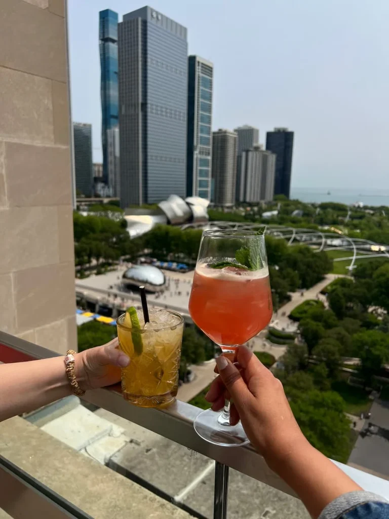 Bejal and Tori doing a cheers with the cocktails, Island Life and Chi Shandy Shake with views ovet Millennium Park and The Bean in the background