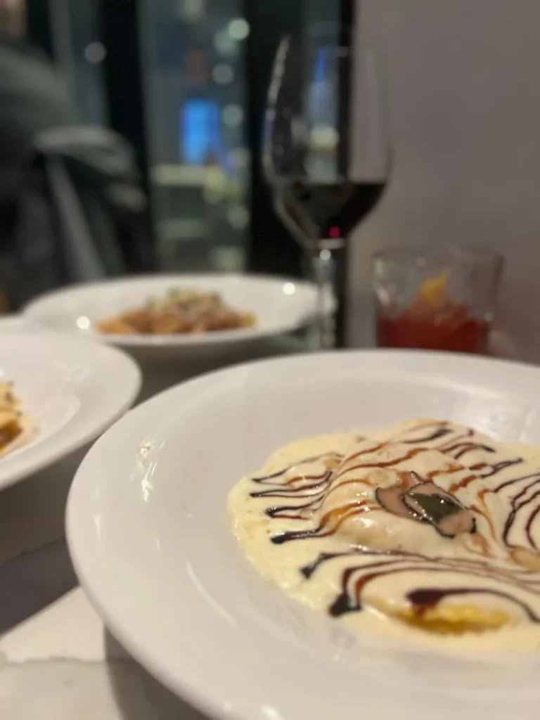 Cool and quirky boutique hotels in Chicago: 4 cheese Ravioli on a white pasta dish with a strawberry fields cocktail in the background. one of the places with vegetarian friendly food in Chicago