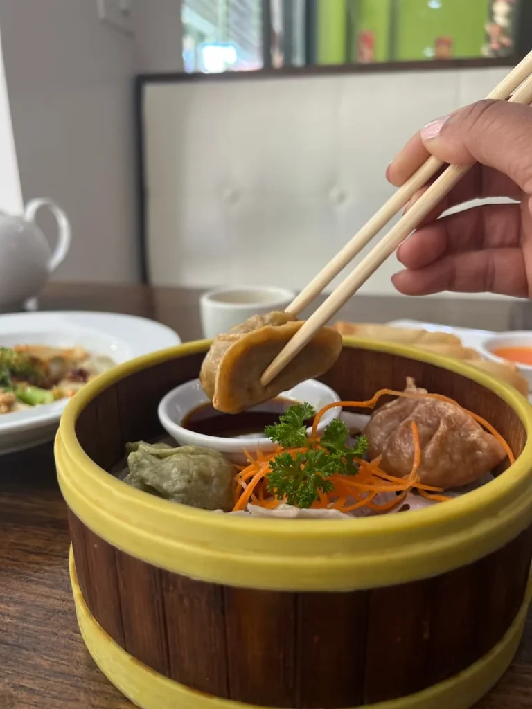 Bejal dipping a spicy dumpling into chilli sauce with chopsticks at veggie House, Chicago
