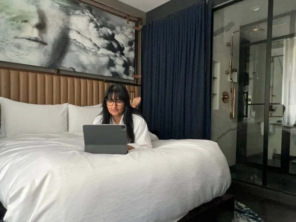 Bejal on bed with dressing gown, working on ipad in the queen room at Hotel EMC2, one of the cool and quirky boutique hotels in Chicago