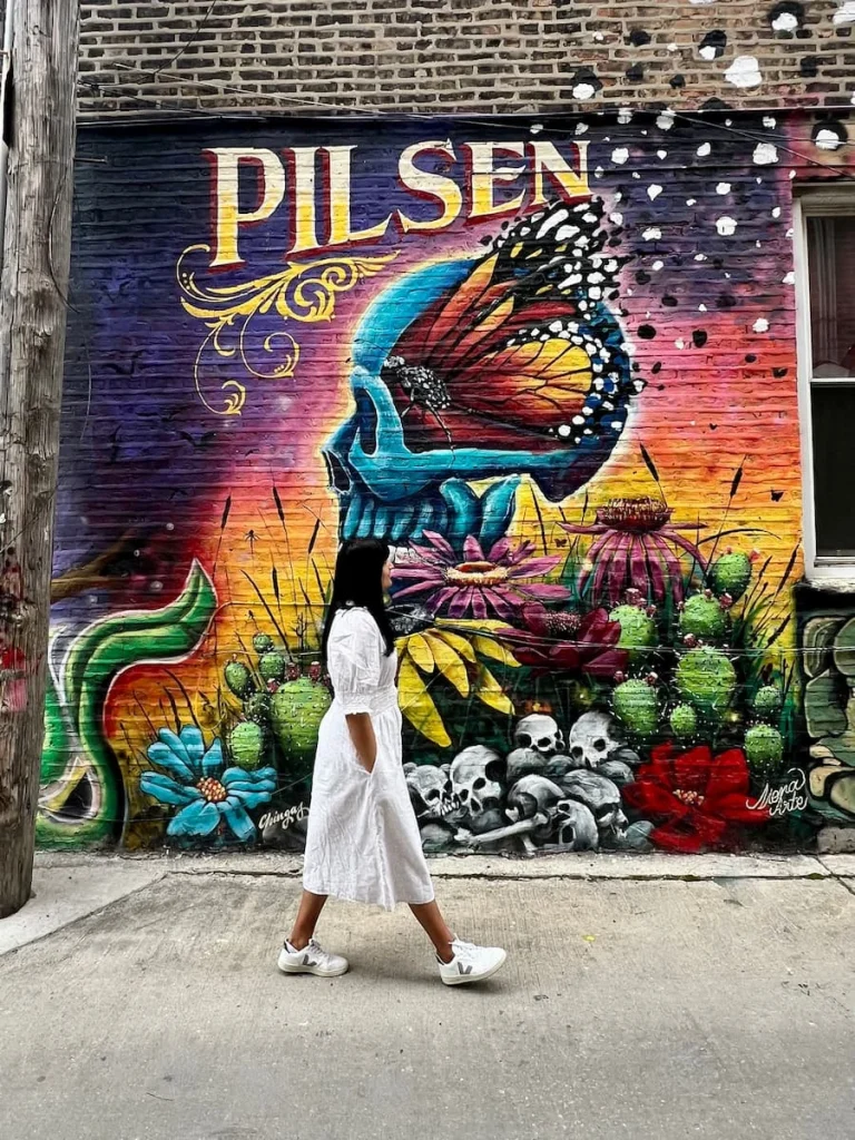 Bejal walking down street with colourful Pilsen graffiti, Pilsen, Chicago. Bejal is wearing a cream and white floral dress with cream sandals. one of non touristy things to do in Chicago