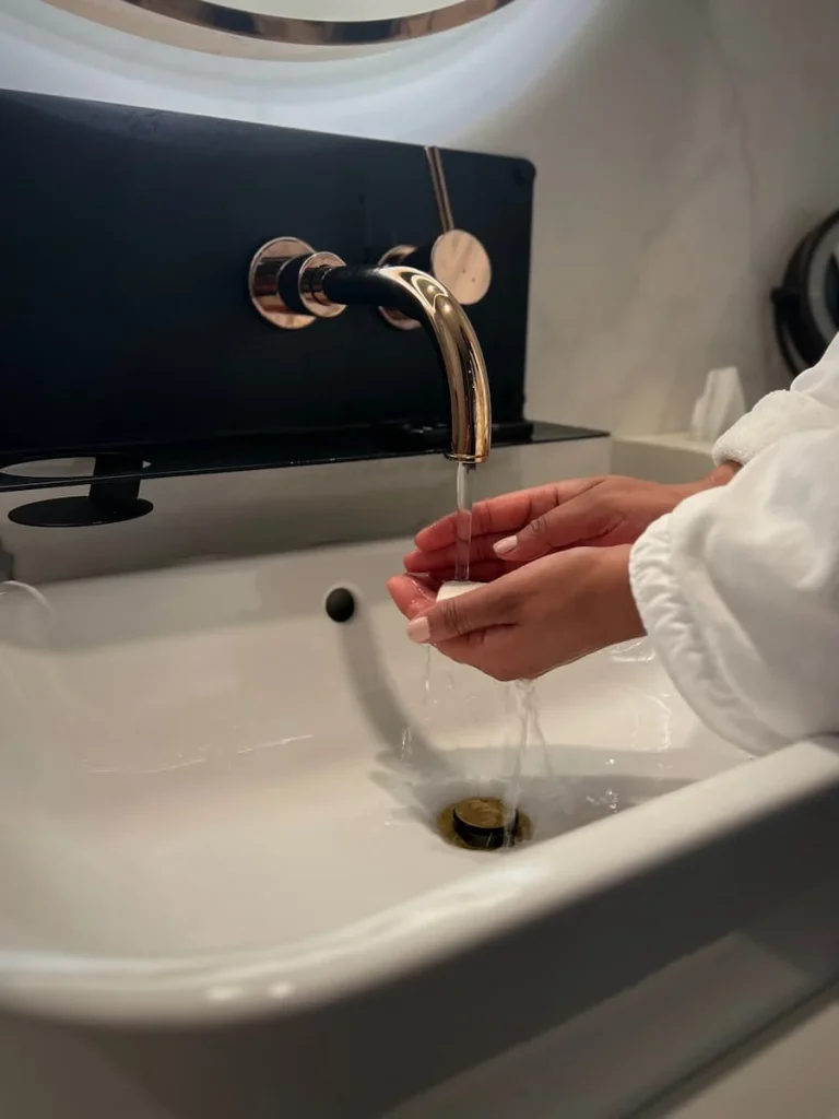 Bejal washing her hands with a white robe and soap on the side, in the bathroom of the Queen Room at HOtel EMC2, one of the cool and quirky boutique hotels in Chicago