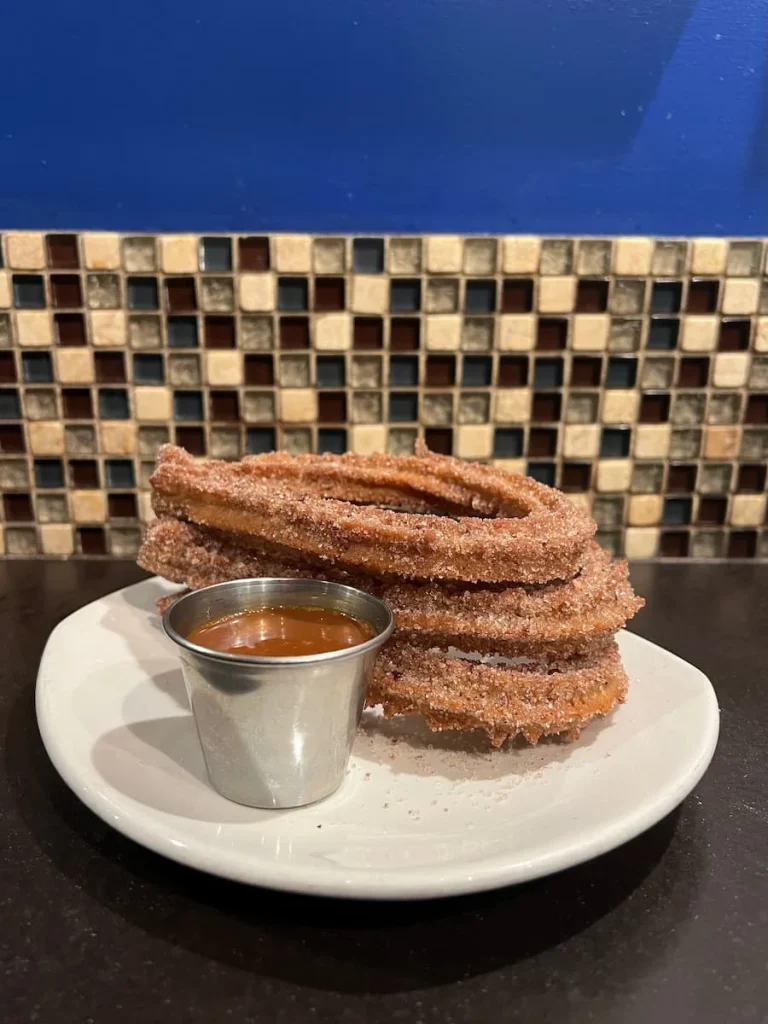 Churros with Cajeta dipping Sauce at XOCO, Chicago. There are a mixtire of mosaic tiles in the background and the wall is painted a bright blue