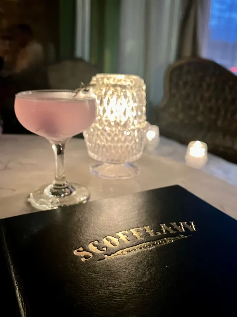 Another Plane Cocktail next to a table light at Scofflaw, Chicago. The darl black and gold menu is also on the table
