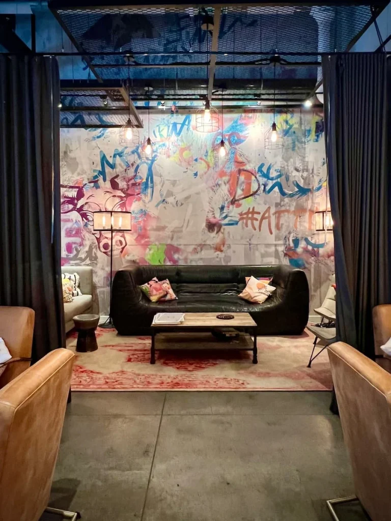Curtained private seating area at Moxy, Chicago. A dark grey sofa with fun scatter cushions, graffiti lettering on the back white wall, cool rugs and chairs with a coffee table. Black curtains surround the space so it can be made private for functions