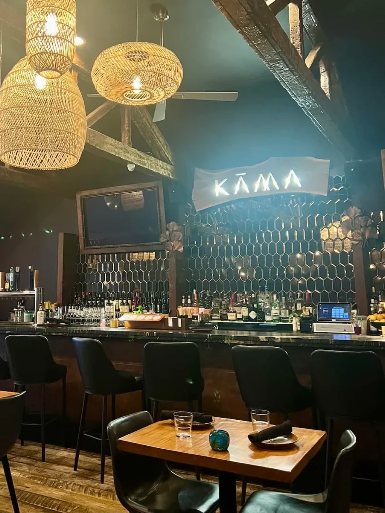 Decor at Kama, Chicago featuring the bar, with spirits, the Kama illuminated sign, tables and chairs in the background