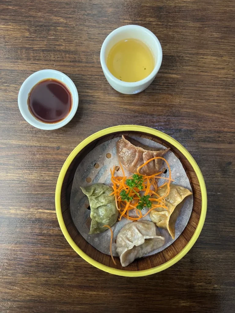 Flat lay photo of a cup of jasmine tea, spcy dumplings with dipping sauce against a dark wood table at Veggie House, Chicago. One of the places that serves vegetarian friendly food in Chicago