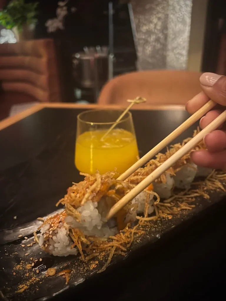 A Mez-Cal Maybe cocktail in the background with bejal picking up a Maki toll with chopsticks at PLANTA queen, Chicago