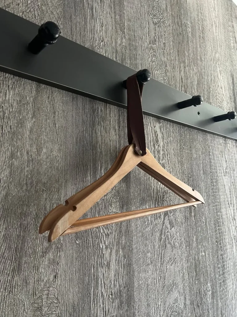 Hanger with brown leather handle at Moxy, Chicago double guest room. Black hooks and a textured grey wallpaper on the walls behind.