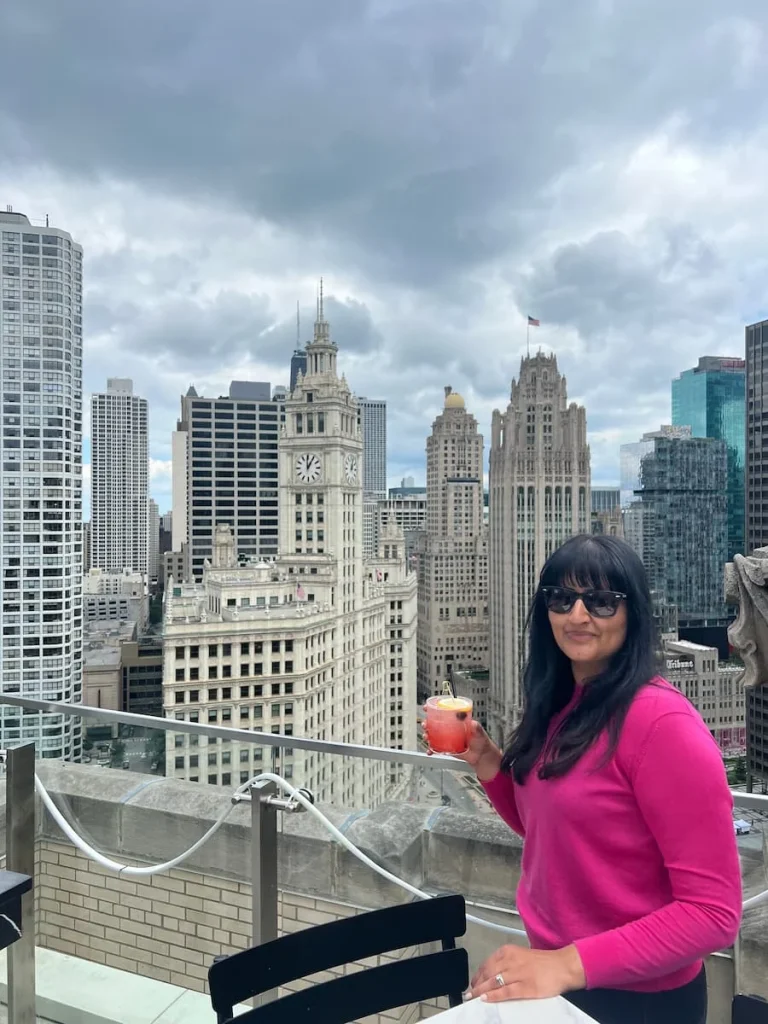 Bejal standing with drink with views of Wrigley Building in the background in Chicago