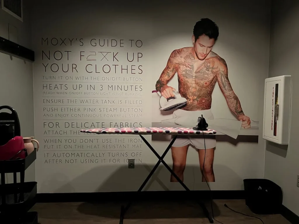 Ironing area artwork at Moxy, Chicago with a topless man ironing and ironing instructions on the wall behind