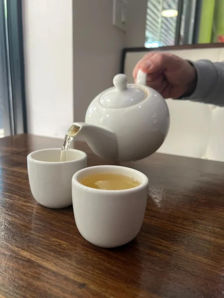 Jasmine tea being poured into 2 white cups with it's pale yellow colour