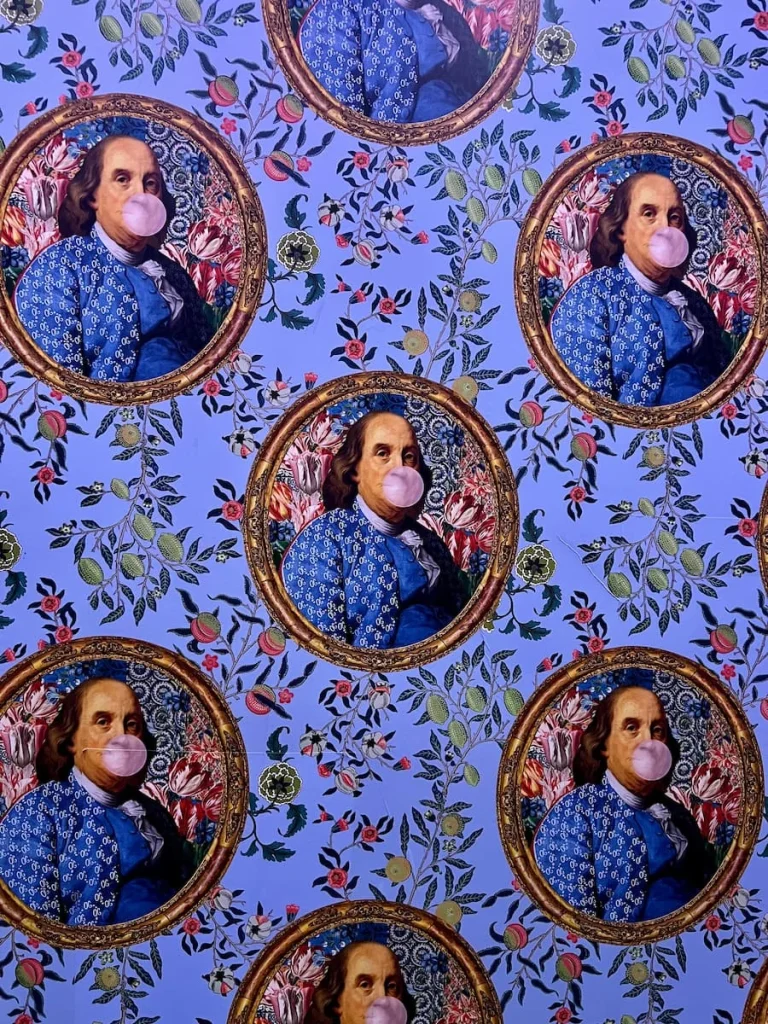 Man blowing a pink bubble gum bubble wallpaper in the lifts wearing a blue jacket in. a circular gold frame and light pink and blue floral background