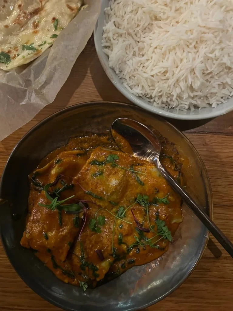 A top lay of the Malay kofta which has. a spoon in it and there is a bowl of plain white rice on the side at Kama, Chicago