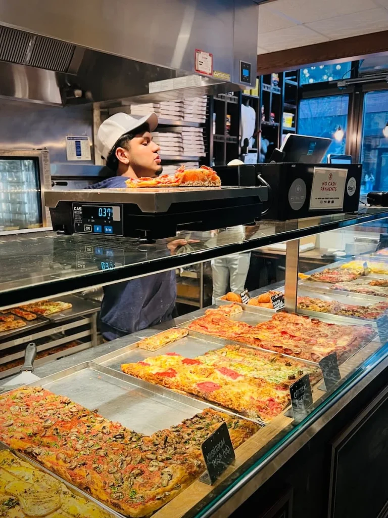 Pizza counter at Bonci in Chicago with server wearing a cap, weighing out pizzas