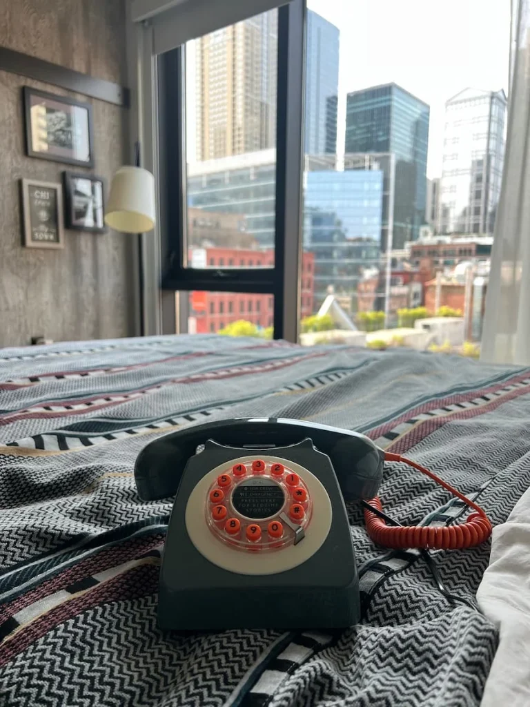 Retro grey and orange telephone on bed at Moxy Chicago with city scape views in the background