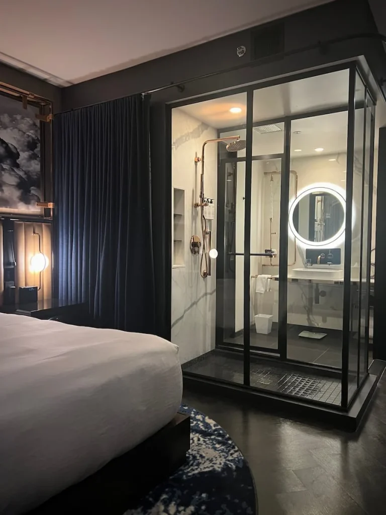 A side view of the shower cubicle in the Queen Room with the reflection of the light rimmed vanity mirror through the glass at Hotel EMC2, one of the cool and quirky boutique hotels in Chicago