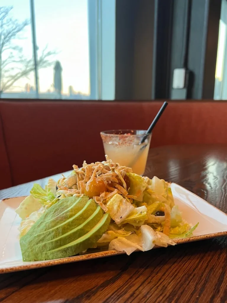 Side view of the Lirica salad with the spicy pineapple Fresno cocktail at Lirica, Chicago. View of the Navy Pier in the background