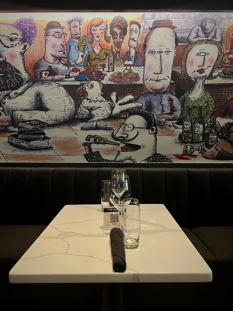 A table setting with artwork behind it and glasses on the table at The Albert Restaurant, Hotel EMC2, one of the cool and quirky boutique hotels in Chicago