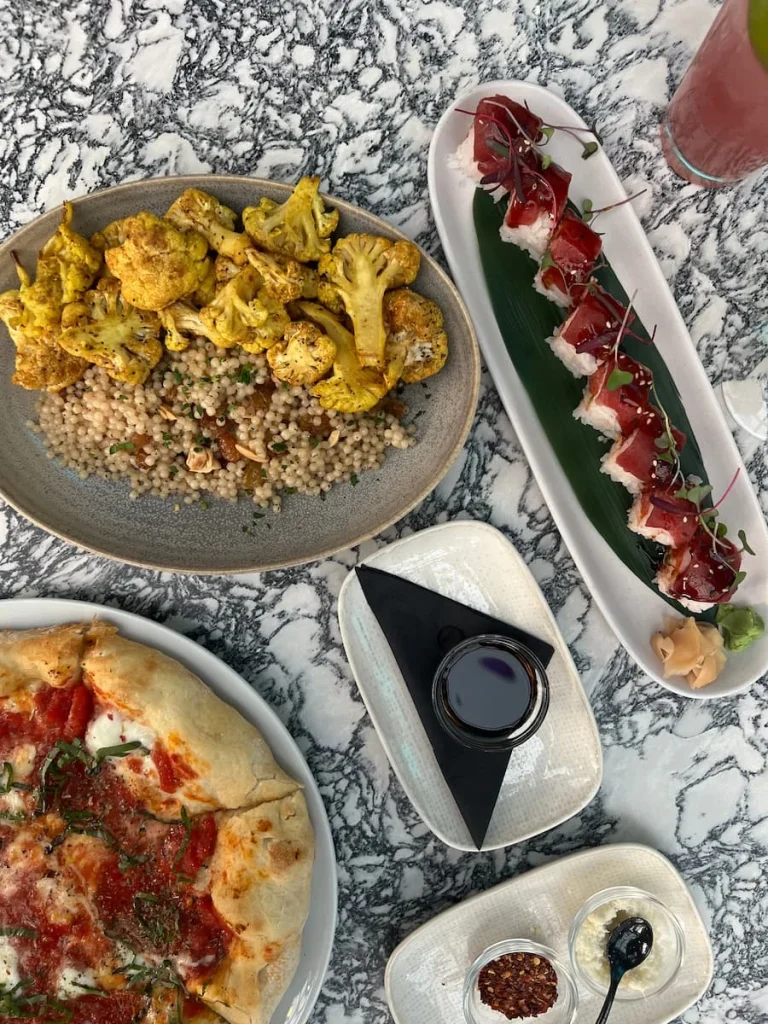 Tap lay of Berry Tequila or Mezcal Sour, curried cauliflower with Israeli couscous, margarita pizza and vegetarian sushi on a grey and white marble effect background at Roof on thewit, Chicago