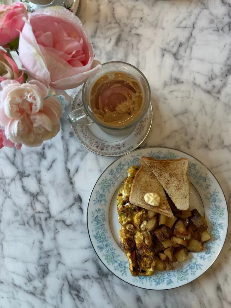Top lay of iced coffee with vanilla syrup and Mexican omelet with potatoes at Sugary, Chicago. The table has some pink and white artificial peony's in a vase and a white and grey marble effect surface