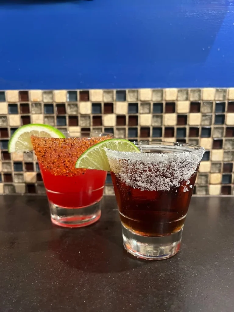 XOCO Margarita and beer at XOCO, Chicago. Both glasses are coated in either salt or spicy seasoning and the back wall has brown and white mosaic tiles and a bright blue wall.