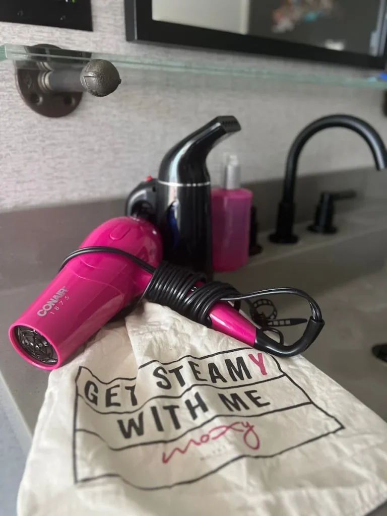 Hairdryer, steamer and bag at Moxy, Chicago on vanity sink area in guest double room