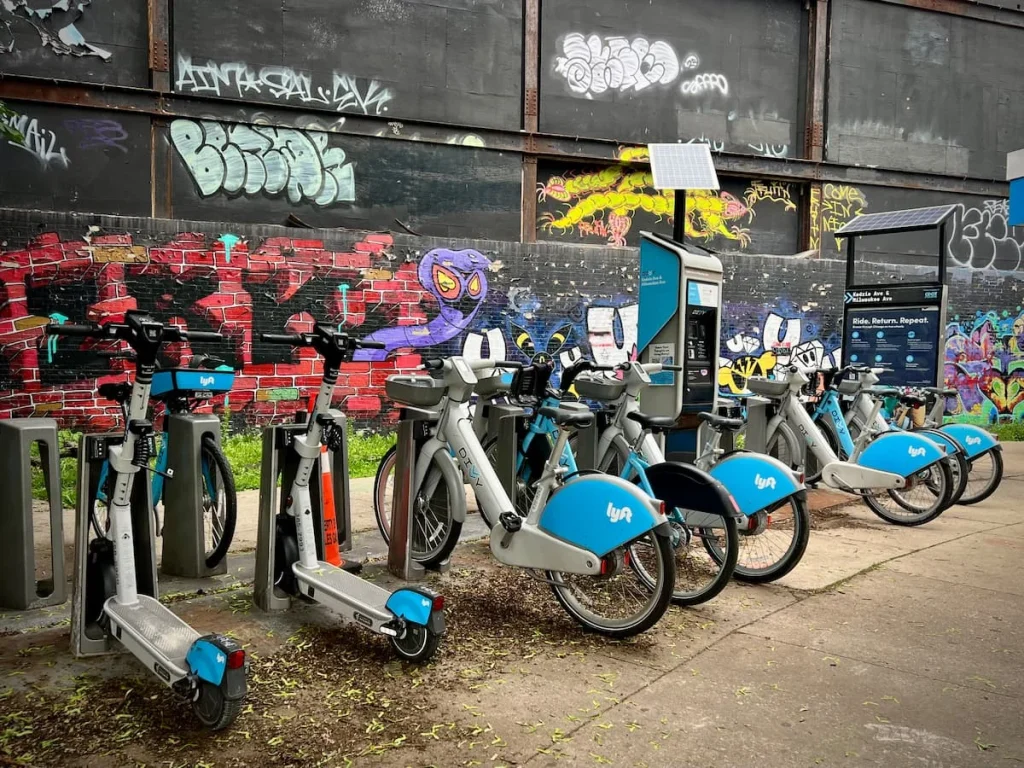 A sustainable guide to Chicago, Divvy Blue bikes in Logan Square against a graffiti background. There are also electric scooters parked next to the Divvy bikes.