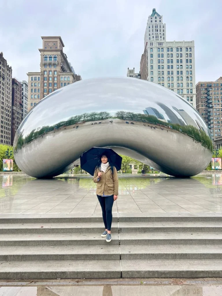 Bejal standing infront of The Bean (Cloudgate) in Chicago with an umbrella in the rain, part of the sustainable guide to Chicago
