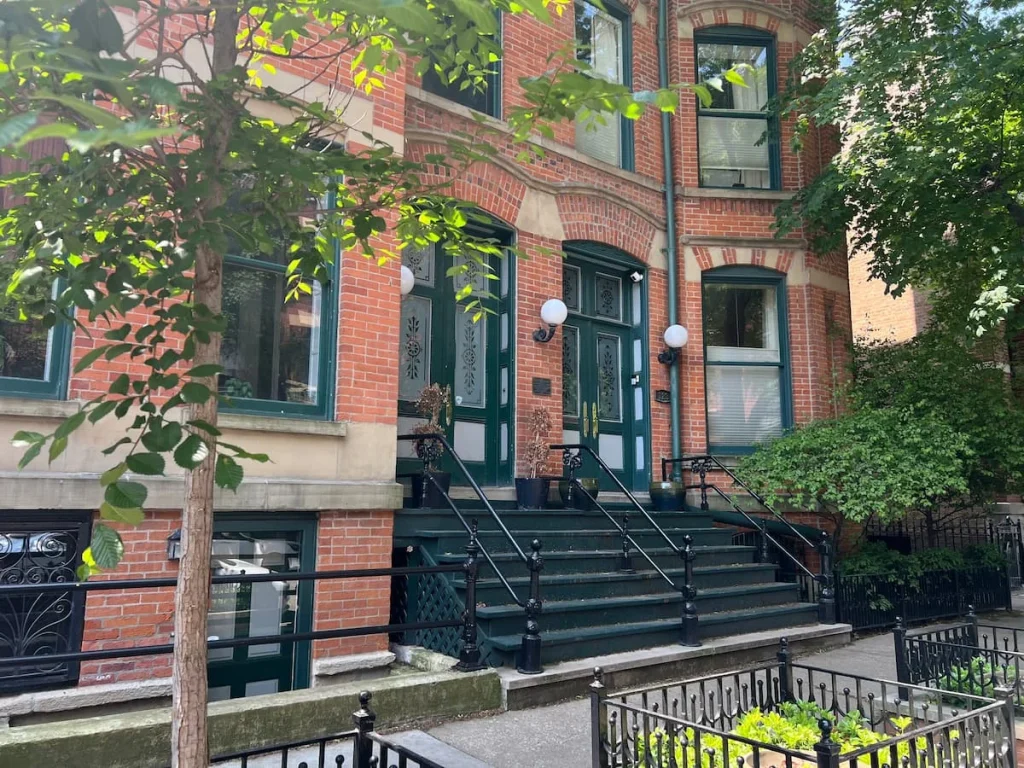 2 large red brick townhouses on a leafy street in teh Gold Coast area of Chicago. They have dark green painted doors and flower beds in front as well as a historic plaque on their fascia.