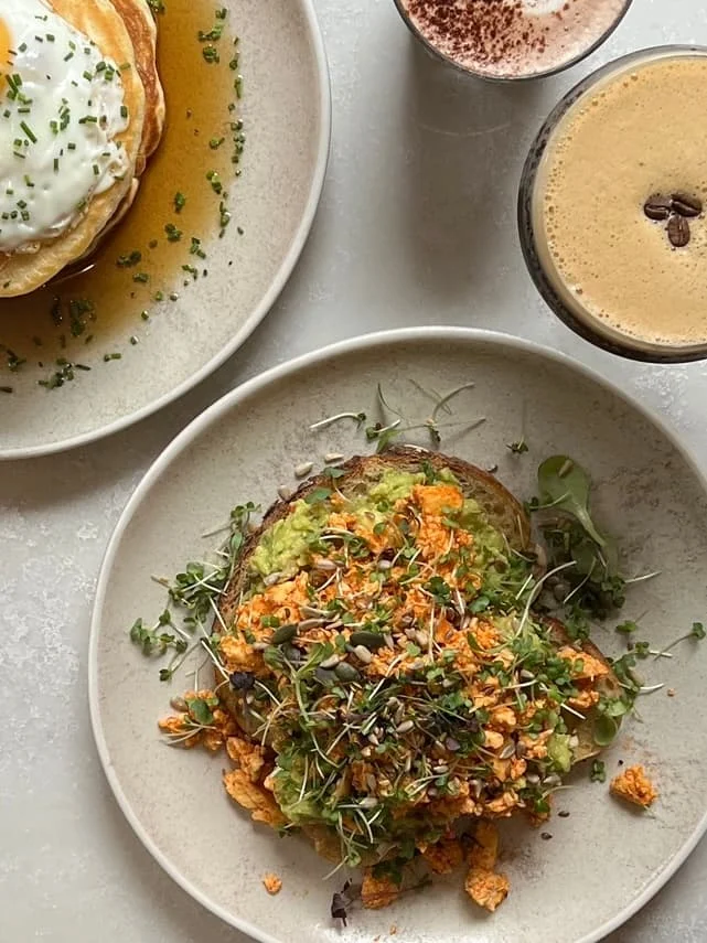 Smashed avocado with sriracha scrambled tofu at Kai, Leicester, with an espresso martini and cappuccino in the corner on a white table.