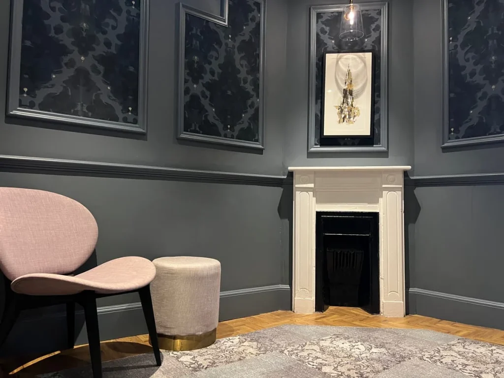 One of the landing areas with a fireplace and light pink chair with a white stool at St Martins Lodge, Leicester