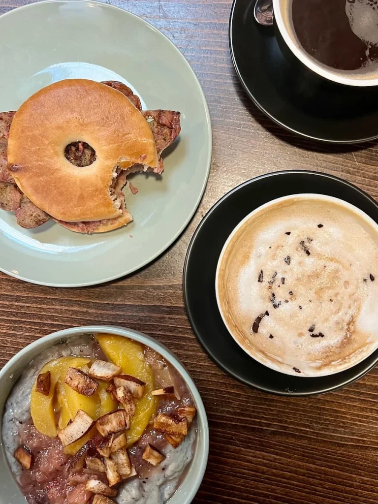 Top lay of Banana porridge with poached mango and coconut plus sausage with pate in a bagel and a cappuccino at Kings Coffee House, Leicester