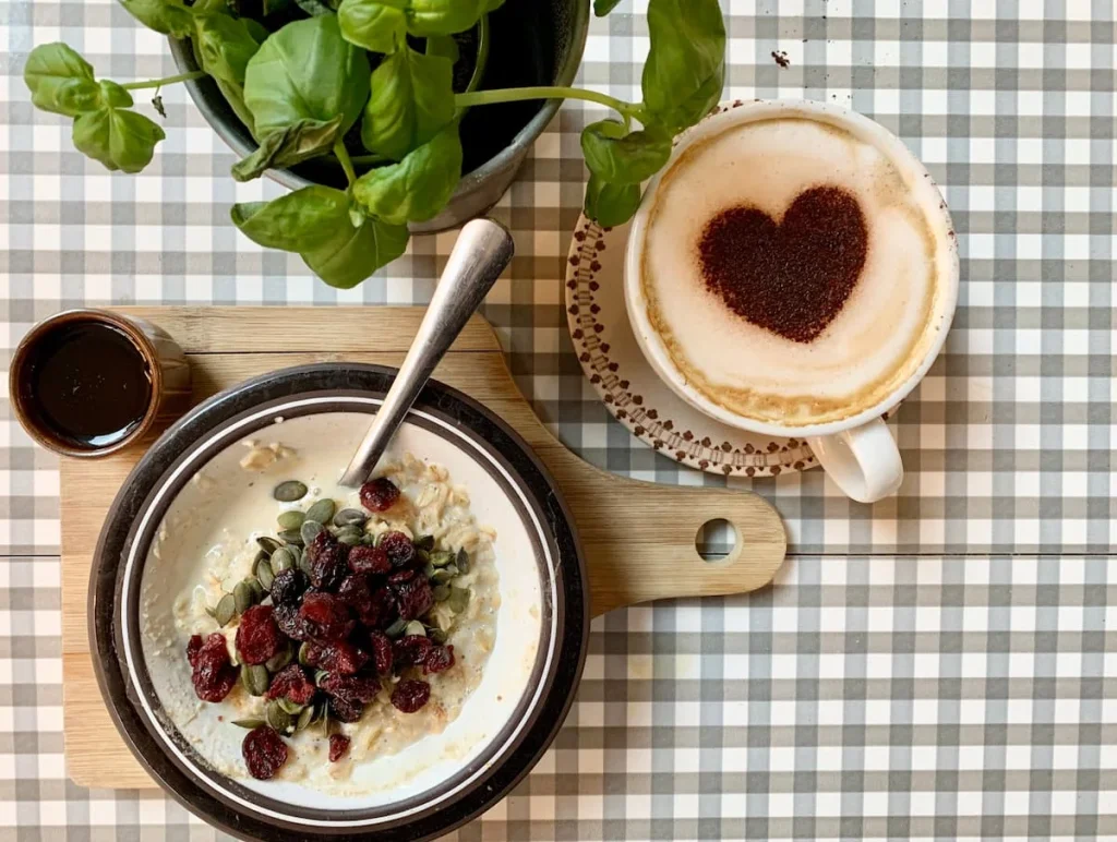 Fruit and porridge top lay with coffee at Bryter Moon Deli in Leicester. The table cloth is a checked grey and white with a light brown board holding a bowl of porridge and fruit