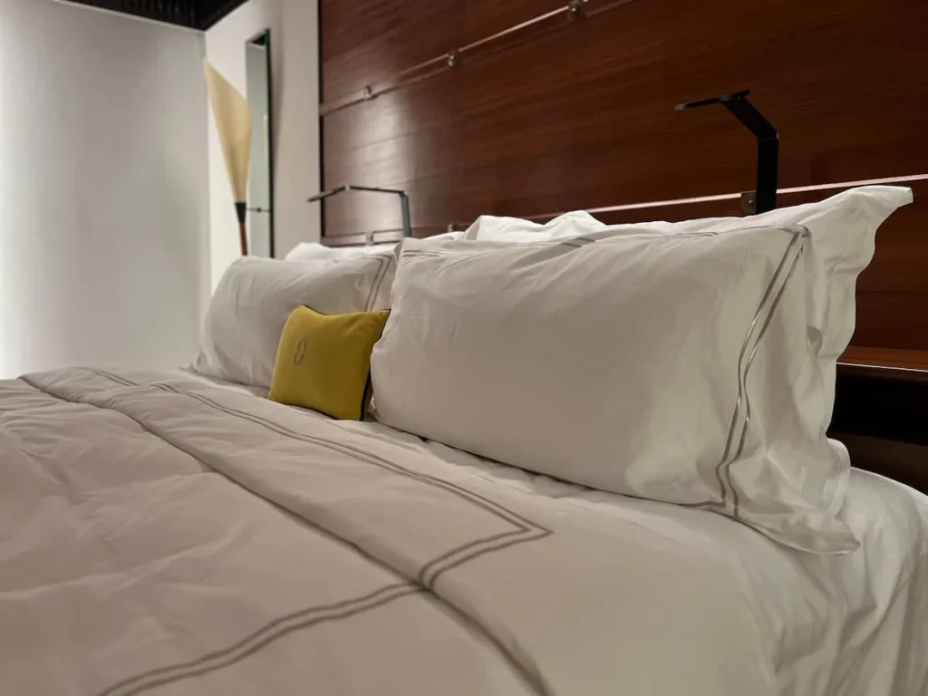 Bed with white duvet and pillowcases with yellow small Datai cushion in the preium room at The Datai Langkawi