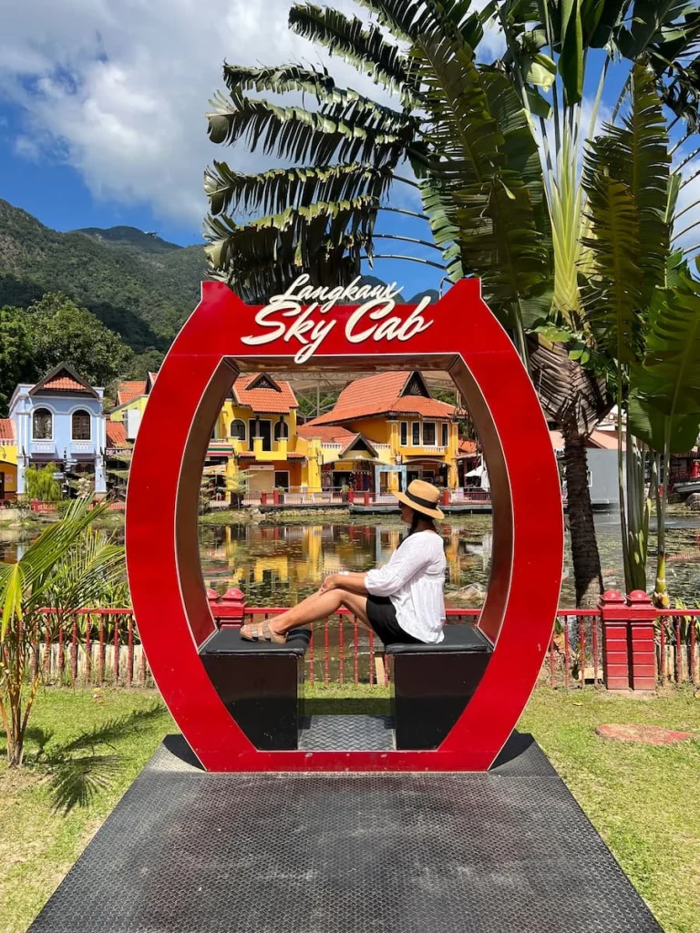Things to do in Langkawi: Bejal sitting in red stationary SkyCab gondola mock-up at Oriental Village.