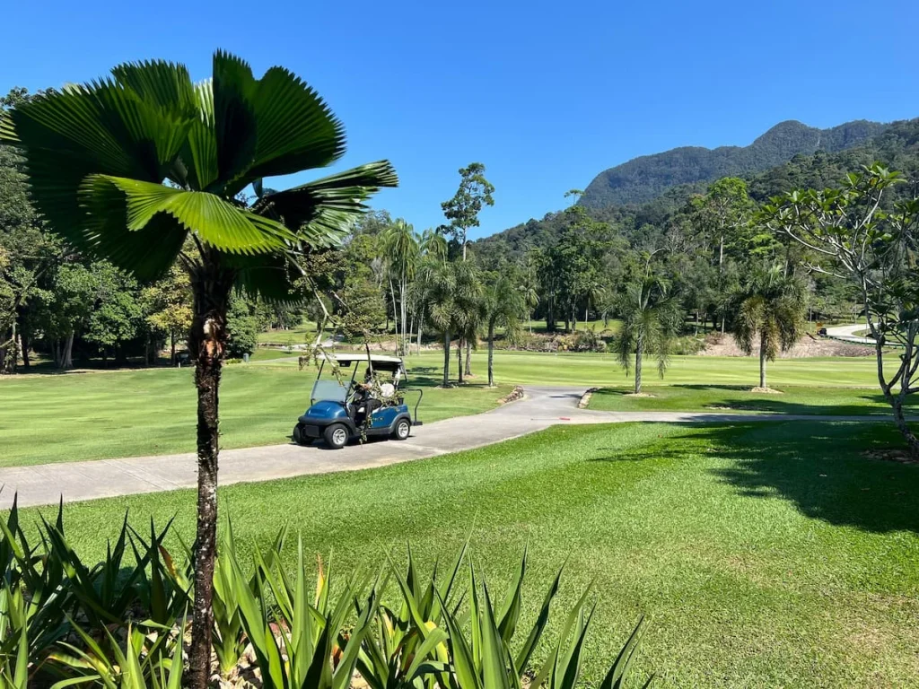 Things to do in Langkawi: Els Club golf course views with tropical trees, mountains and gof buggy's driving by in Langkawi
