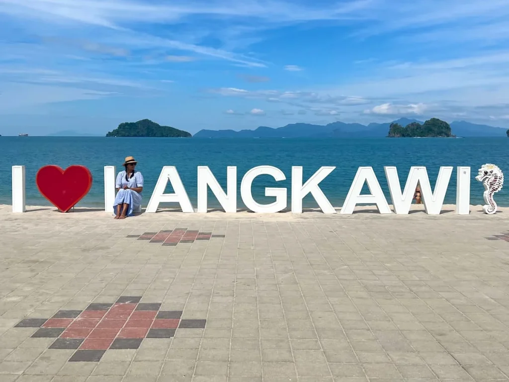 THings to do in Langkawi: I love Langkawi sign at Tanjung Rhu beach with Bejal sitting on 'L' in a blue and white checked dress