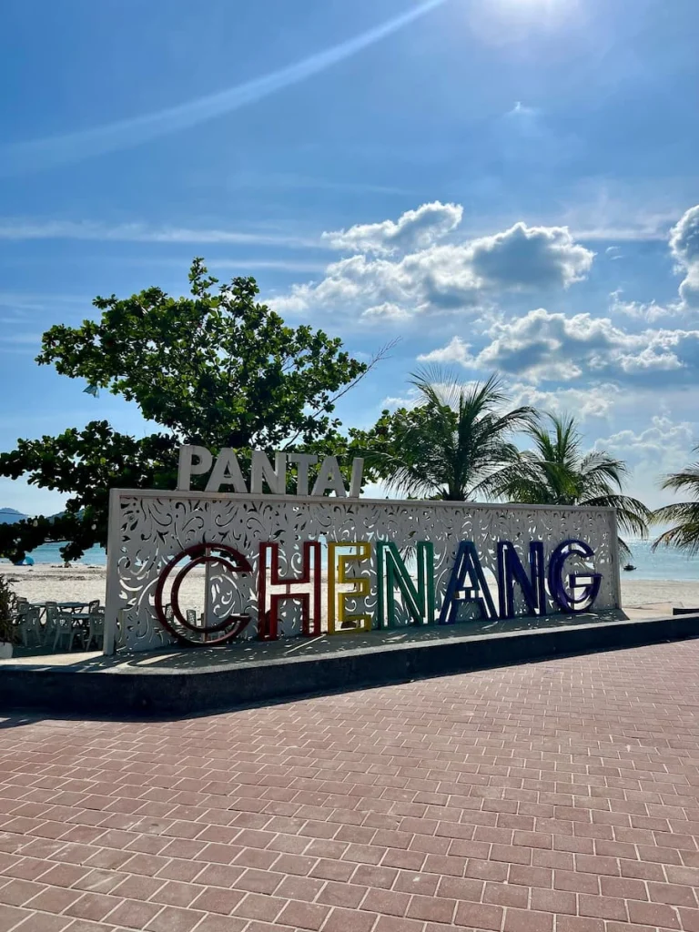 Things to do in Langkawi: Pantai Cenang Beach sign with palm trees and beach in the background in Langkawi