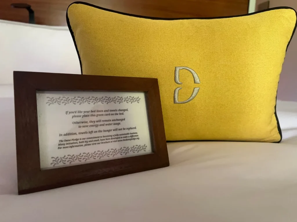 Eco-friendly hotels in Langkawi: Saving water by not washing linens daily sigh on bed with yellow Datai cushion in the background