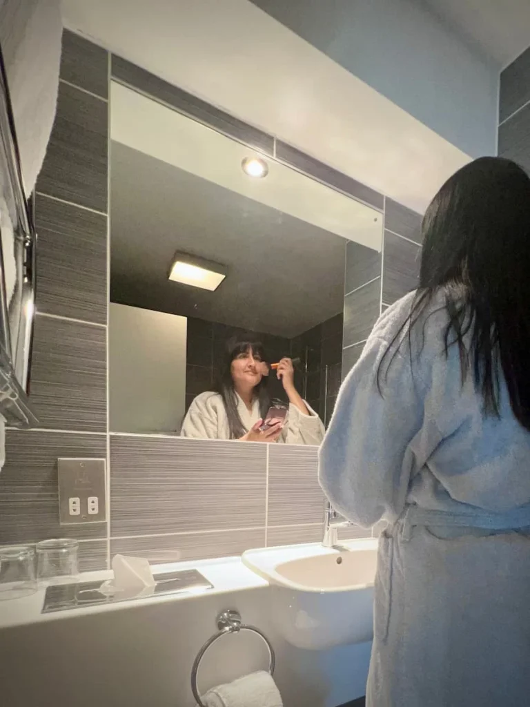 Bejal putting on make-up in the bathroom in robe in Chancellor's Room, Burleigh Court HOtel, Loughborough