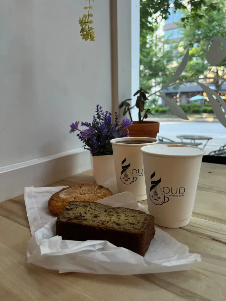 Banana and walnut bread plus the house scone on a ledge with a cappuccino and drip coffee in white Oud cups next to a plant at Oud Coffee, Chicago