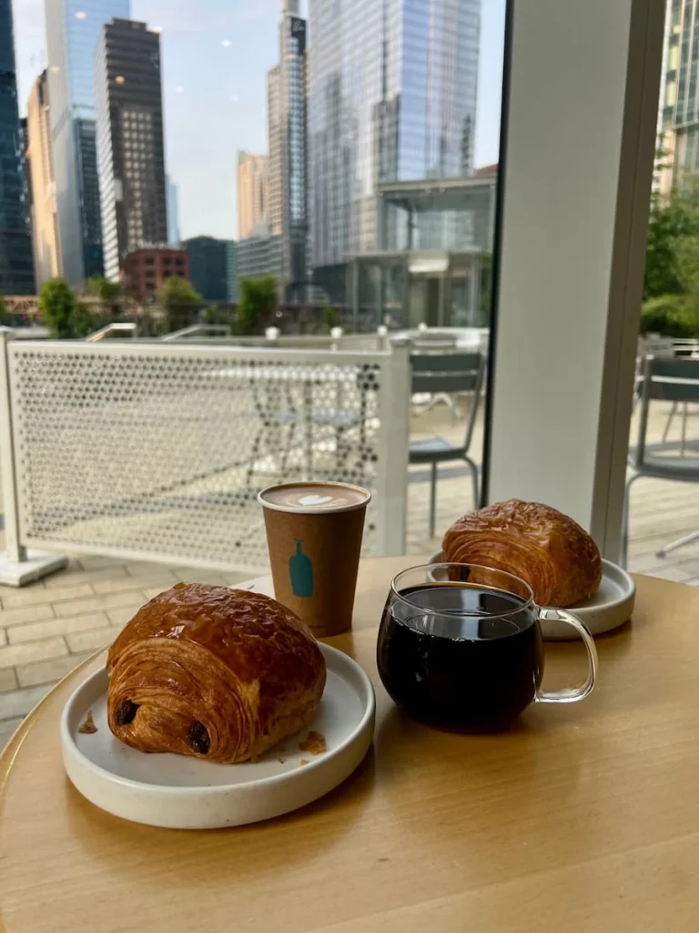 Two Pain au chocolat with a cappuccino in a paper cup and a drip black coffee in a transparent cup overlooking the Chicago River at Blue Bottle Coffee, Chicago